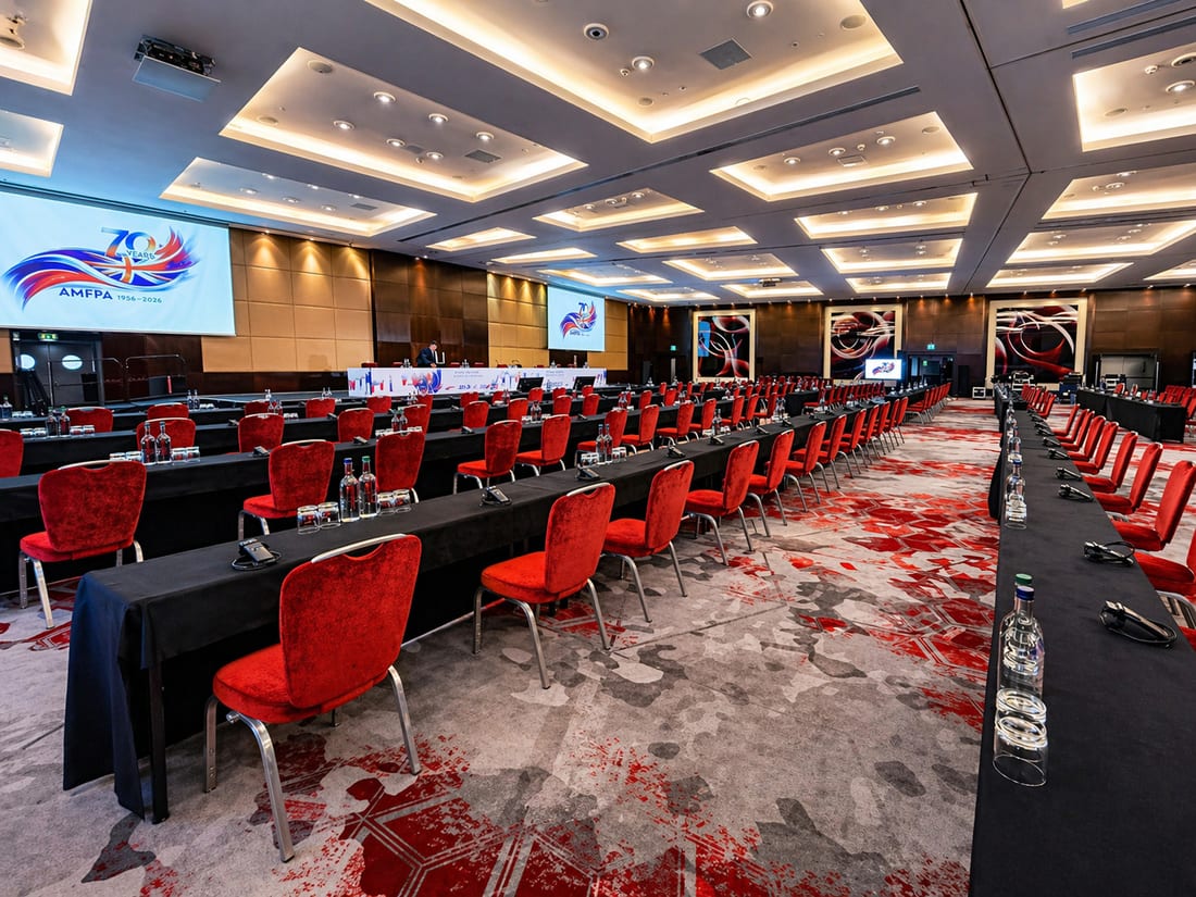 Conference room set in cabaret rows with red chairs and branded screens for an international annual conference
