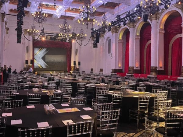 Grand chandelier ballroom set with round tables and a stage for a London gala dinner