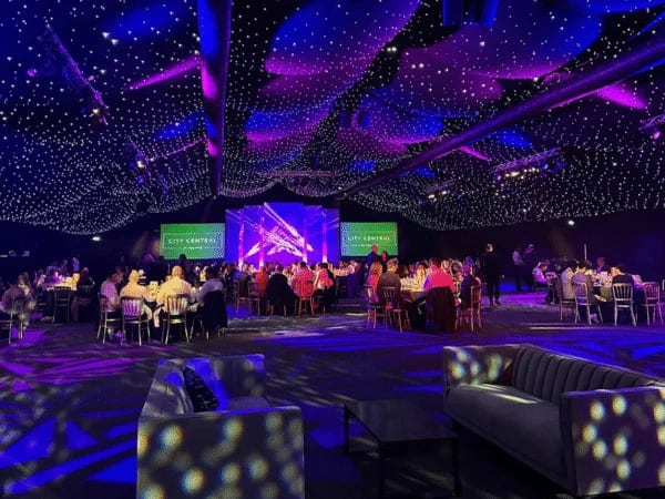 Large gala dinner under a starlit ceiling with a stage, screens and lounge seating